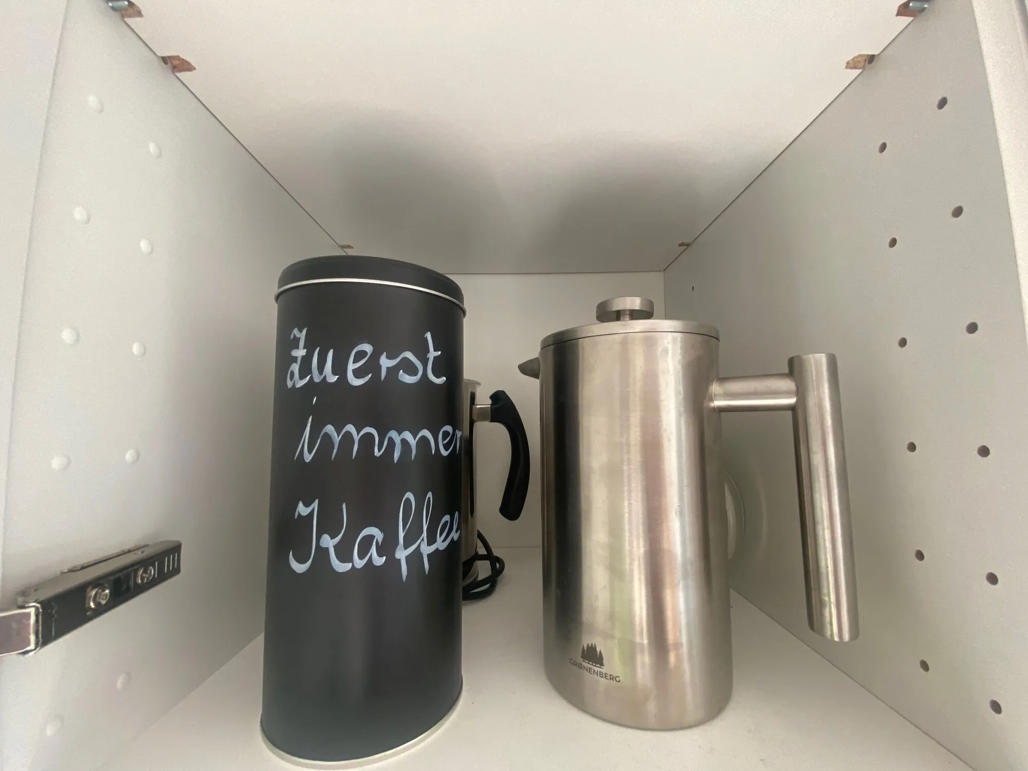 Kaffeekanne und Dose mit der Aufschrift „Zuerst immer Kaffee“ im Regal